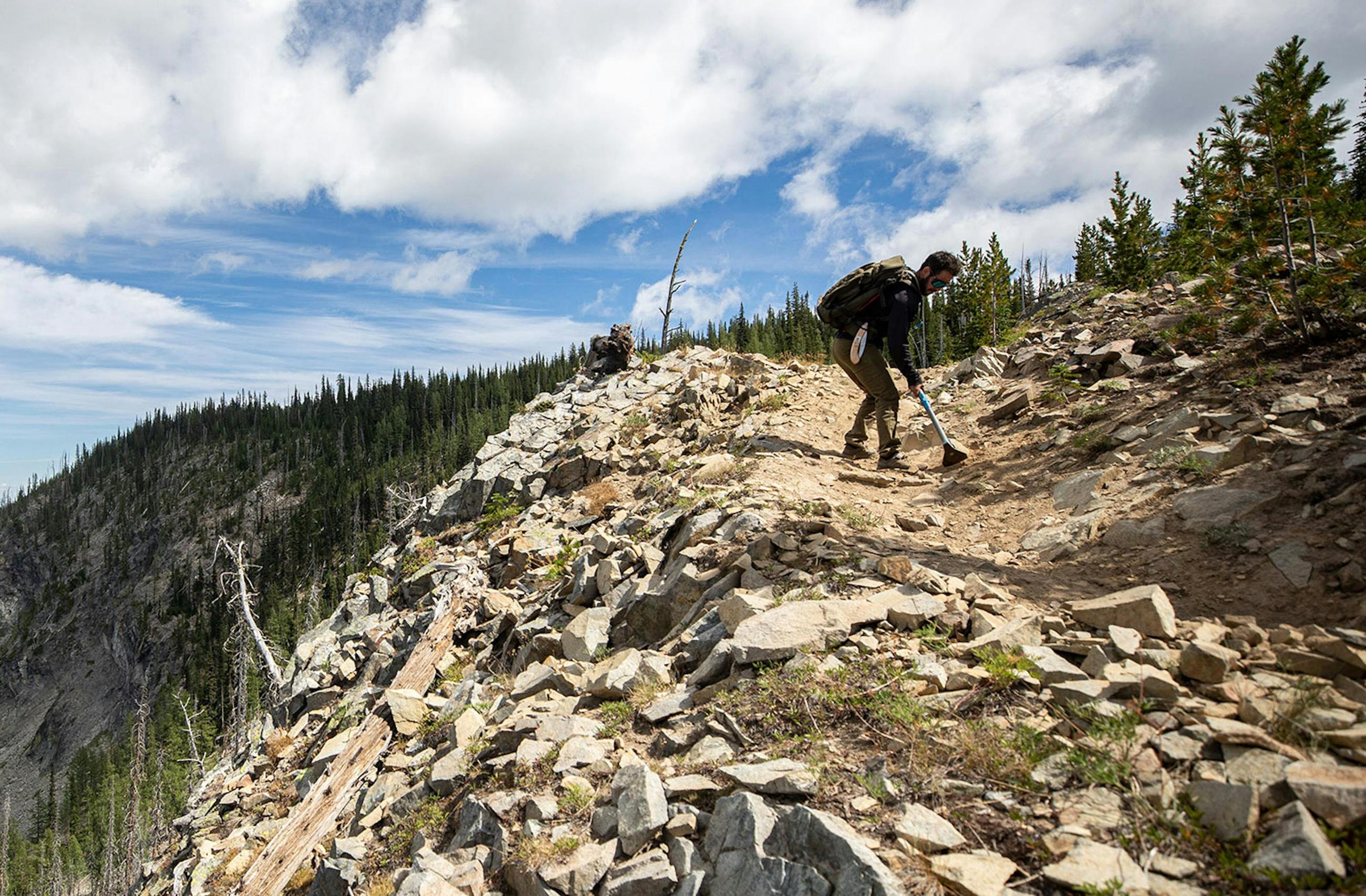 Paydirt Banner - A trail builder moving rocks on a dusty single track trail